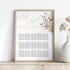 a wedding seating chart on a shelf next to a vase with dried flowers in it