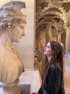 a woman standing next to a busturine in a room filled with marble sculptures