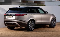 the rear end of a silver range rover parked in front of a white wall and building