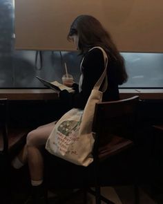 a woman sitting at a table with a book and a tote bag on her lap