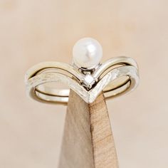 a close up of a ring on top of a wooden stand with a pearl in the middle