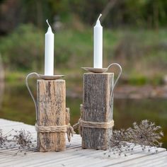 two white candles are sitting on some wood