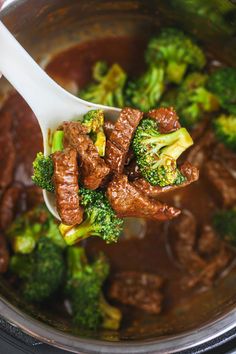 beef and broccoli being stirred in a slow cooker with a ladle