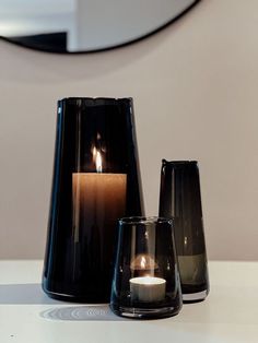 three candles sitting next to each other on top of a white table with a mirror in the background