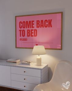 a white chair sitting next to a table with a lamp on it in front of a pink poster