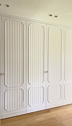 an empty room with white closet doors and hard wood flooring on the side wall