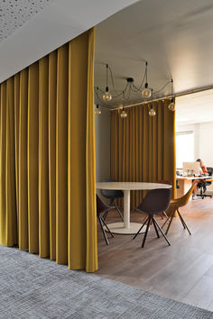 a room with yellow curtains and chairs around a white table in front of a large window