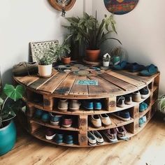 a round wooden table with many pairs of shoes on it and plants in the corner