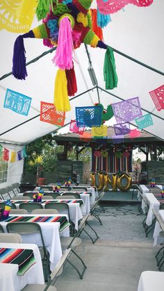 tables and chairs are set up under a canopy with colorful tassels hanging from the ceiling