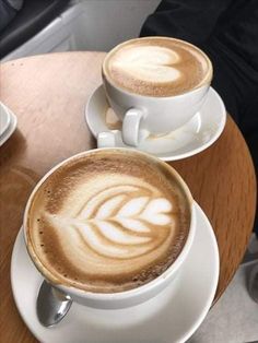 two cups of cappuccino sitting on top of a wooden table