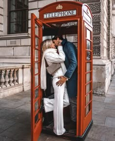 a man and woman kissing in a red phone booth on the side of a street