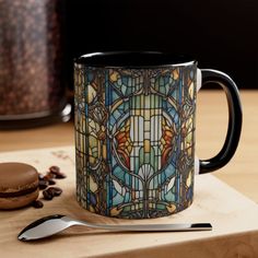 a stained glass coffee mug sitting on top of a wooden table next to a spoon