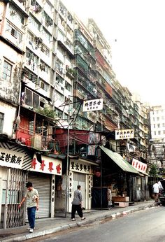 people are walking down the street in front of some buildings with signs on them and hanging from balconies