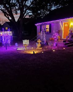 a house decorated for halloween with purple lights and decorations on the front lawn at night