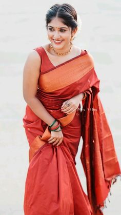 a woman in an orange sari is standing on the beach and smiling at the camera