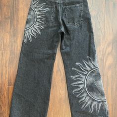 a pair of jeans with embroidered sun and moon designs on them sitting on a wooden floor