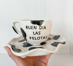 a hand holding a coffee cup and saucer with writing on the bottom, in front of a white background