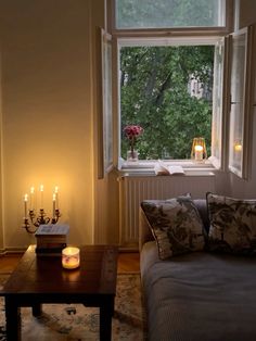 a living room filled with furniture next to a window and lit candles on the coffee table