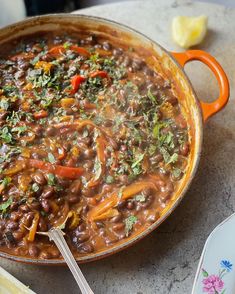 a pot filled with beans and vegetables on top of a table next to utensils