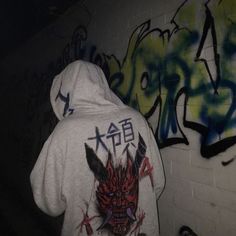 a person wearing a hoodie standing in front of graffiti covered wall with writing on it