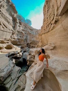 a woman sitting on top of a rock next to a canyon filled with water and rocks