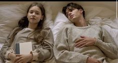 two people laying in bed next to each other and one is holding a book while the other holds an open book