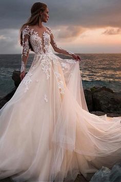 a woman in a wedding dress is standing on the rocks near the ocean with her back to the camera