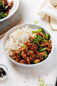 two bowls filled with rice, broccoli and chicken on top of a table