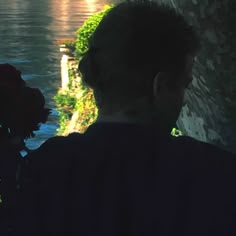 a woman standing next to a body of water with flowers in her hair and wearing a black shirt