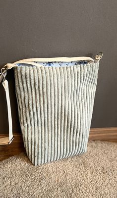 a white purse sitting on top of a carpeted floor next to a gray wall