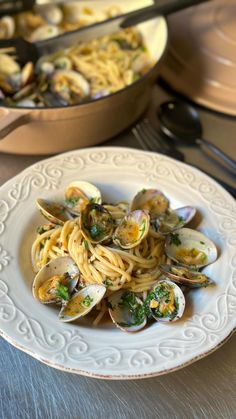 a plate of pasta with clams and broccoli on it next to a skillet