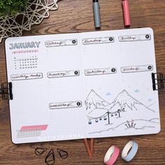 an open planner with markers and pencils next to it on a wooden table top