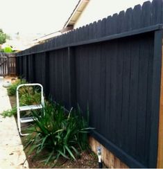 a white lawn chair sitting next to a black fence and green plants in front of it