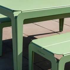 two green plastic tables sitting next to each other on a sidewalk with tile flooring