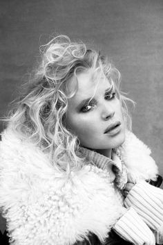 a black and white photo of a woman with curly hair wearing a fur collared coat