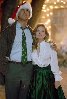 a man and woman dressed in christmas attire standing next to each other with lights behind them