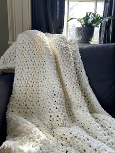 a white crocheted blanket sitting on top of a couch next to a window