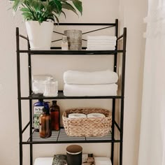 a bathroom shelf with towels, soaps and other items on it next to a potted plant