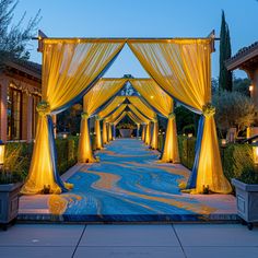 an outdoor wedding venue with yellow drapes and blue carpeted walkway leading to the entrance