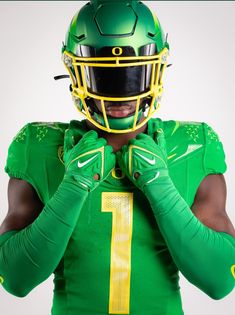 a football player wearing a green uniform and holding his hands to his face with one hand