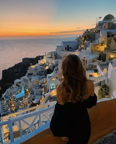 a woman standing on top of a balcony looking at the ocean and buildings in the background