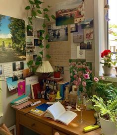 a wooden desk topped with lots of books next to a window covered in pictures and plants