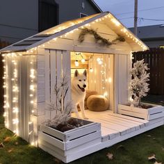 a dog house is decorated with christmas lights and decorations on the outside, while a large white dog stands in it's doorway