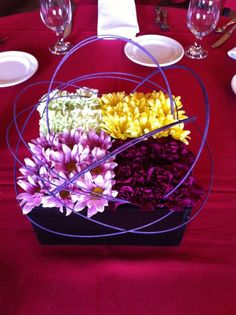 a table topped with plates and flowers on top of a red cloth covered tablecloth