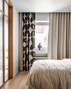 a bed sitting next to a window in a room with wooden floors and curtains on the windowsill