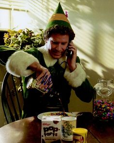 a man dressed as elf is talking on his cell phone at the dining room table