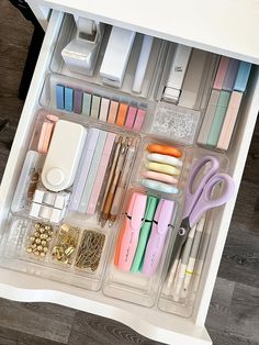 an organized drawer filled with pens, scissors and other office supplies on top of a wooden floor