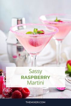 two martinis with raspberry and mint garnish in them on a table