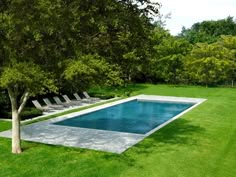 an empty swimming pool in the middle of a lush green yard with lounge chairs around it