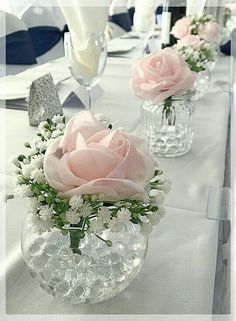 several vases filled with pink roses and white flowers on a long table set for an event